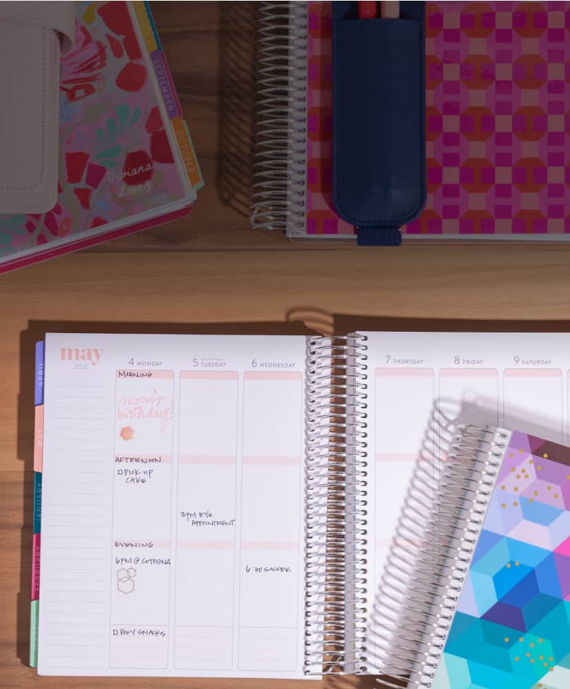 two lifeplanners. One open showing vertical layout with writing inside. One closed lifeplanner stacked on top featuring geometric design.