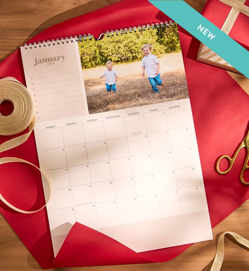 New photo calendar on a white wall featuring a family photo. Calendar hangs over wooden desk set up. Click to shop photo calendars.