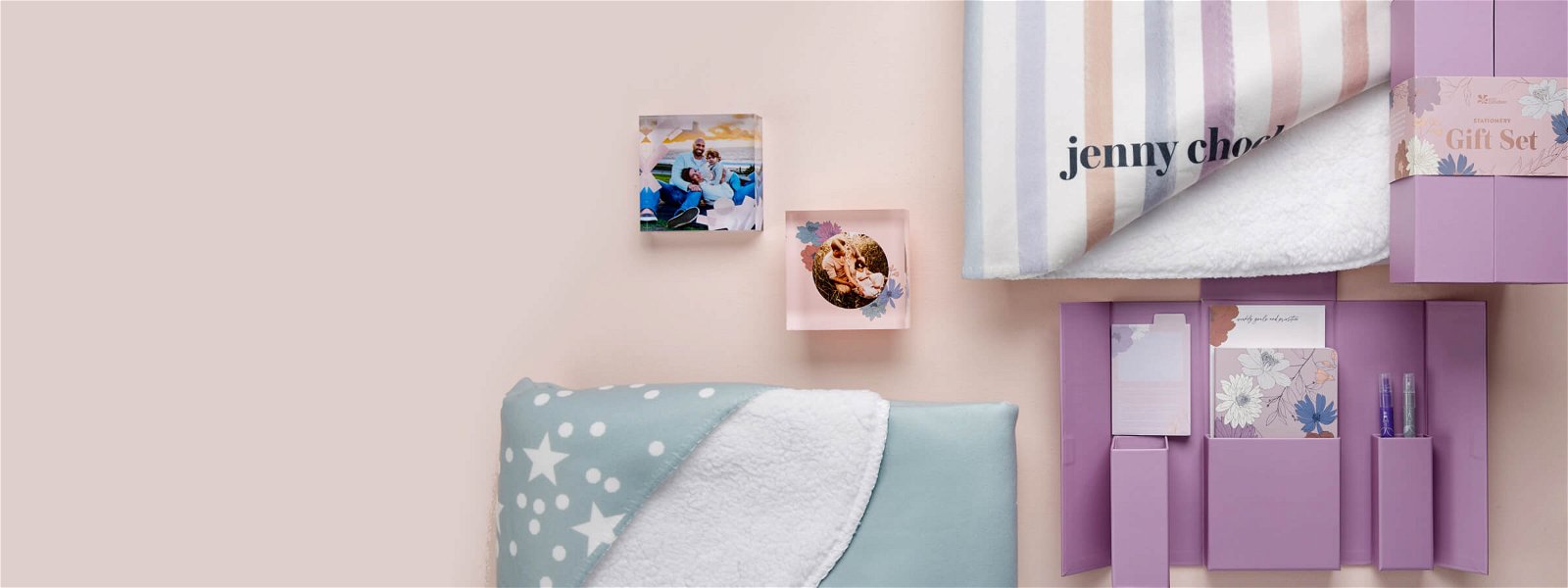 An overhead desk scene of personalized sherpa throws, acrylic blocks featuring family photos and stationery gift sets.