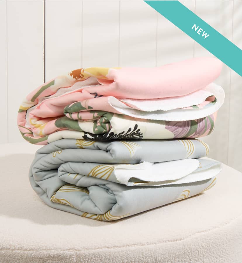 Stack of folded sherpa throw blankets on a fuzzy ottoman in a well lit room.