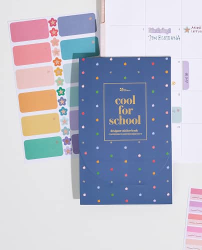 closed Took Cool For School sticker book on top of coiled planner showing monthly spread with assorted stickers and writing inside.