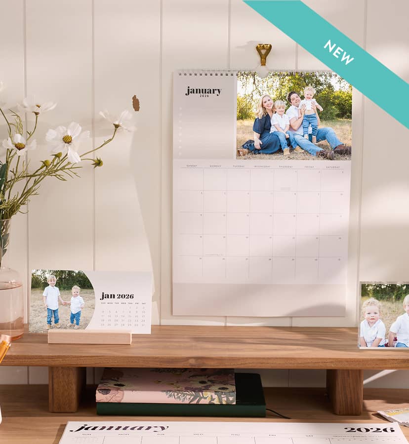 New photo calendar on a white wall featuring a family photo. Calendar hangs over wooden desk set up. Click to shop photo calendars.