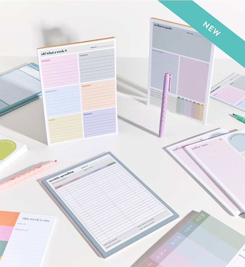 Flat lay of spiral-bound planners, notebooks, and notepads on a pink background, featuring colorful designs, gold accents, and organizational layouts.