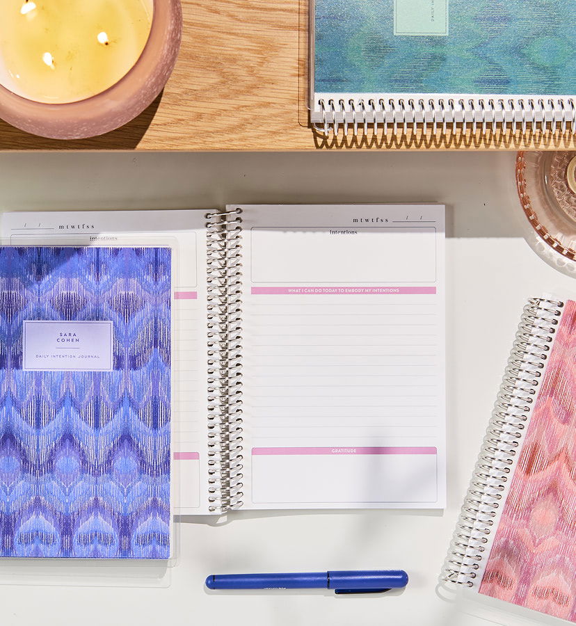  Custom Wall Calendar hung over a wooden desk with plants and a cup filled with pens. Click to shop custom wall calendars.