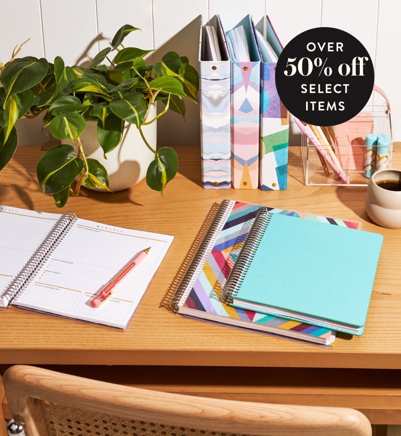 over 50% off select items. Coiled notebooks and journals on a wooden desk with accessories