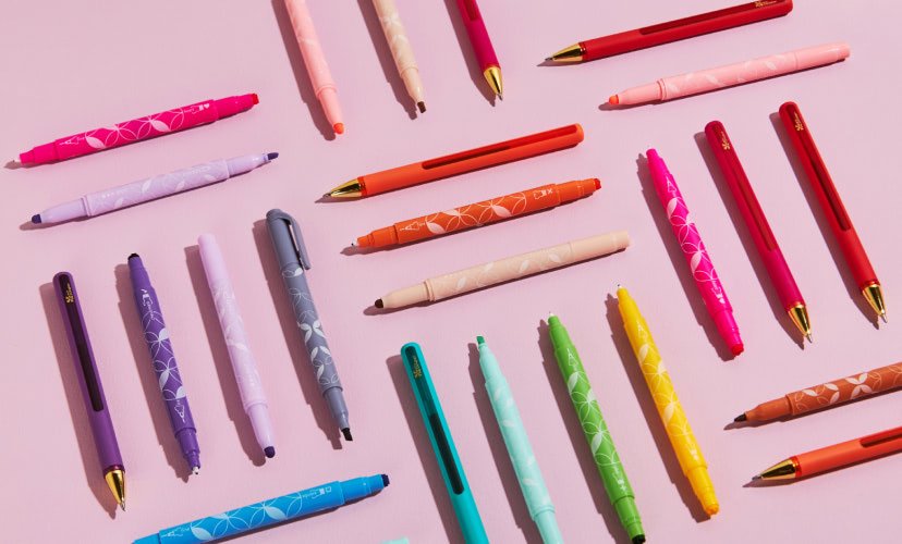 Colorful collection of pens and markers on a pink background