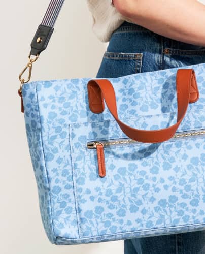 woman holding a blue floral tote bag on her shoulder.