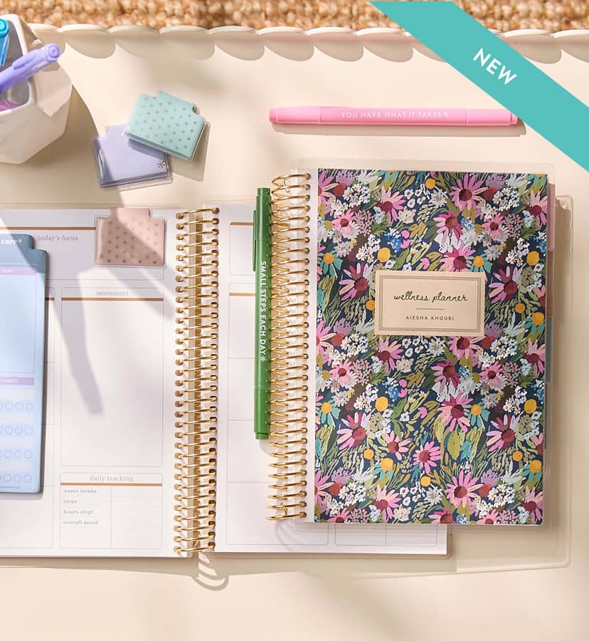 new coiled wellness planner featuring floral design and colorful accessories on a white desk. Click to shop new planners and journals. Click to shop now.